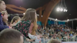 Plan rapproché sur un jeune femme dans le public de l'Arena Stade Couvert de Liévin, acclamant les athlètes qui rentrent sur la piste lors du Meeting de Liévin 2024.