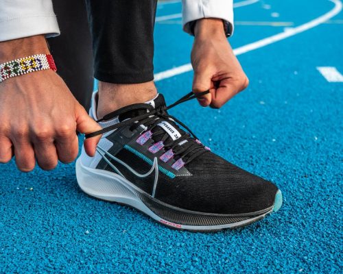 Zoom sur les pieds d'un homme faisant ses lacets, avec une paire de Nike Zoom Pegasus 38 au pied. Il est sur une piste d'athlétisme en tartan bleu.